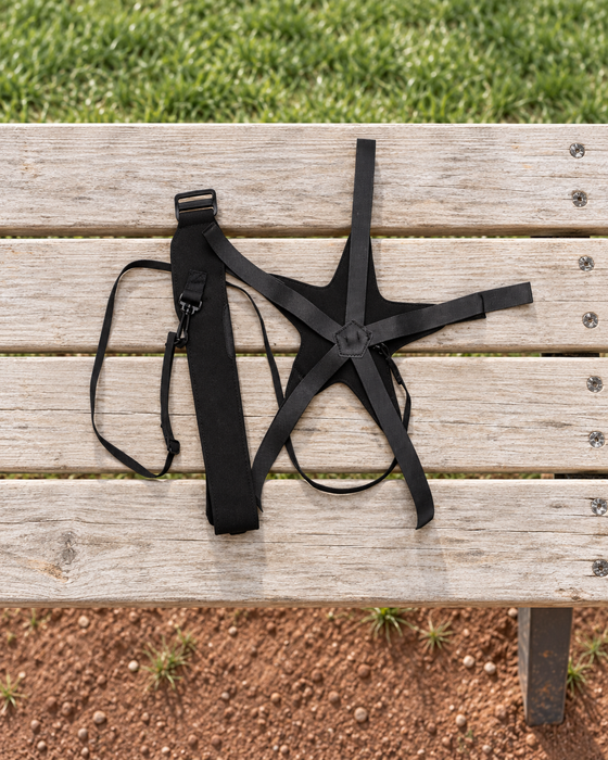 Black soccer training belt and ball harness laid out on a wooden bench beside grass.