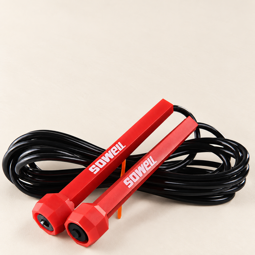 Red jump rope with polygonal handles and black coiled cord on an ivory surface
