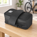 Black bicycle saddle bag with mounting strap on a wooden bench, with a bicycle blurred in the background.