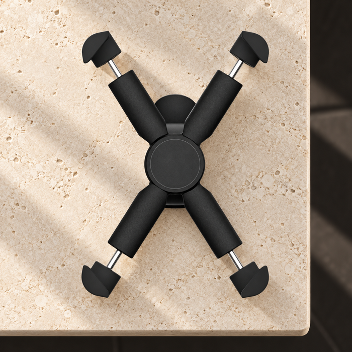 Black four-arm phone holder resting on an ivory stone console.