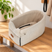 Beige pet car seat with a black inner tether on a wooden entryway bench.