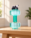 Green dumbbell-shaped water bottle with a dark lid and white flip spout on a wooden bench.