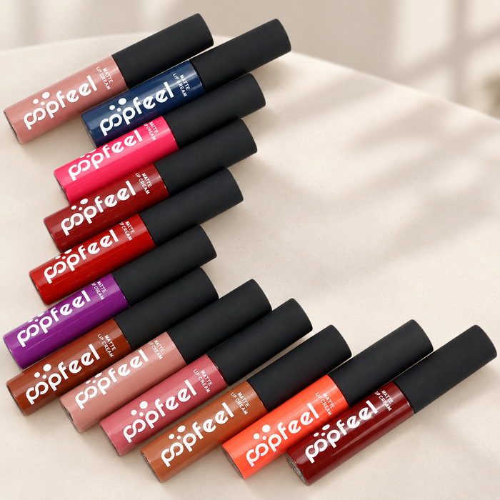 Twelve colourful matte lip cream tubes with black caps on an ivory surface.