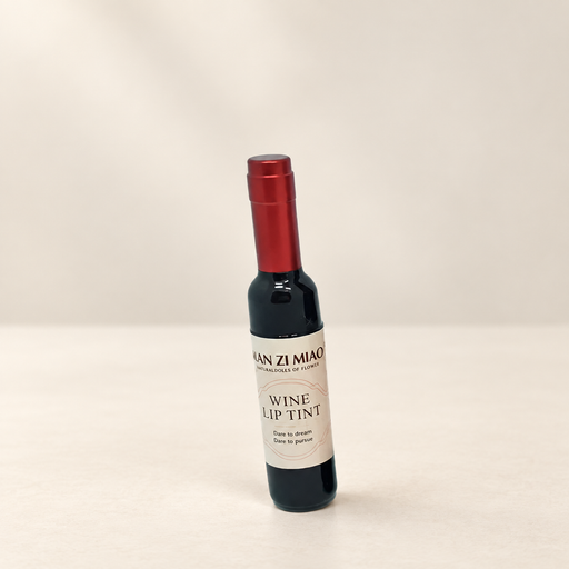 Wine-bottle-shaped lip tint with a red cap and cream label on an ivory surface.