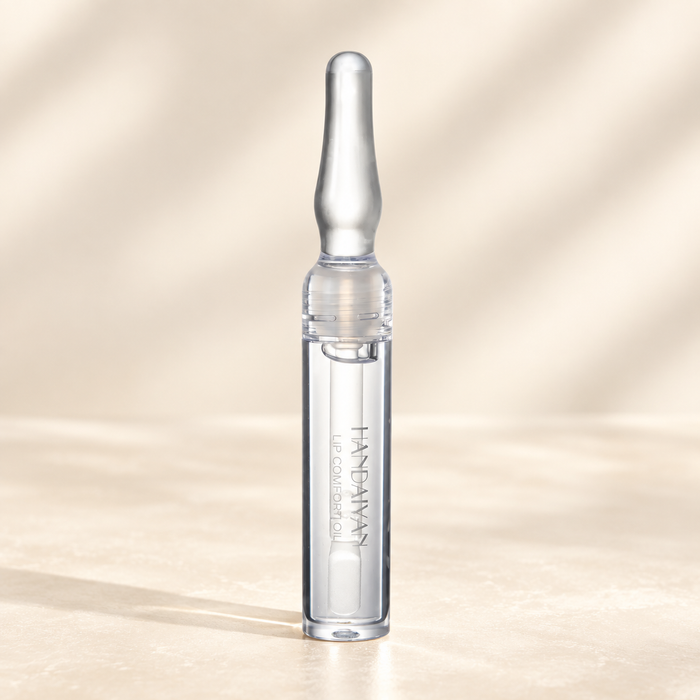 Clear lip oil tube with a silver cap on an ivory surface