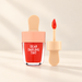 Peach-capped red lip tint with a separate applicator view on an ivory surface.