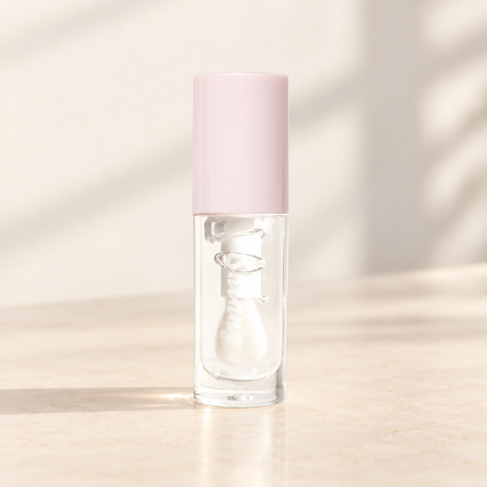 Clear lip gloss tube with pale pink cap on ivory vanity.