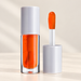 Orange liquid lip product with grey caps and applicator on ivory surface.