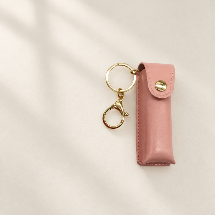 Dusty-pink lipstick carrying case with a gold key ring and clasp on ivory.