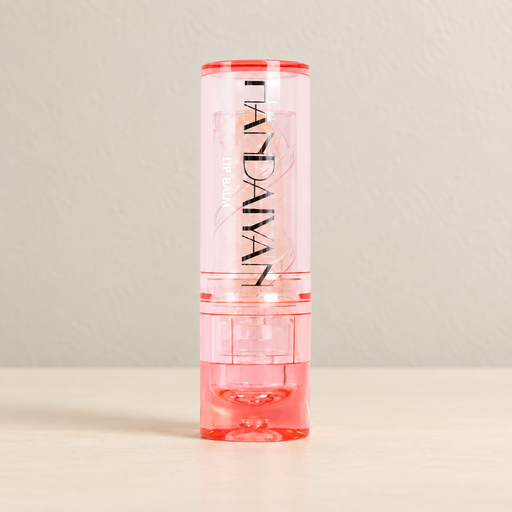 Transparent pink capped lip balm on an ivory surface