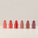 Six miniature lipsticks arranged by shade on an ivory surface