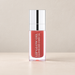 Peach pink lip oil in a clear bottle with silver cap on ivory