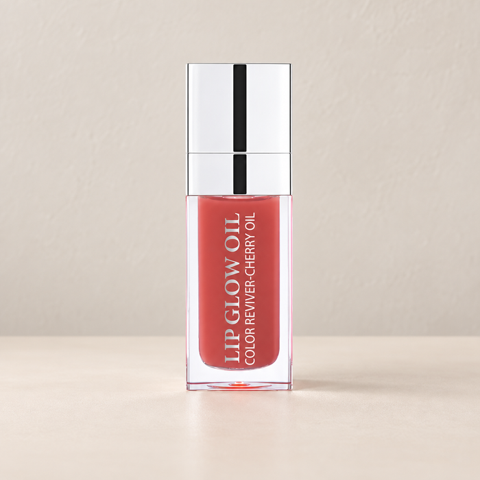 Peach pink lip oil in a clear bottle with silver cap on ivory