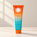 Orange and turquoise sunscreen tube on an ivory surface.