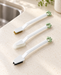 Three white cleaning brushes with green hanging loops on an ivory kitchen counter.