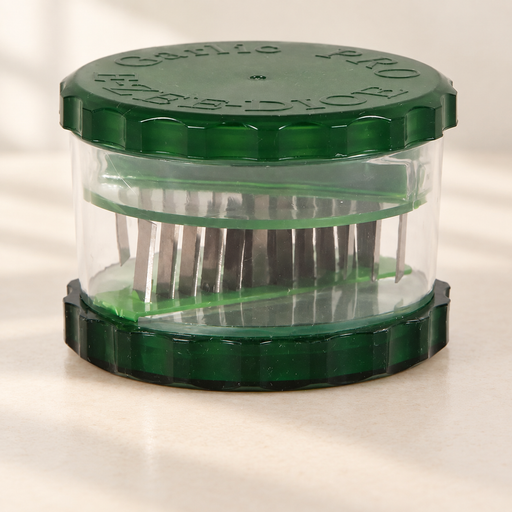 Transparent garlic cutter with dark green lid and base on an ivory surface.
