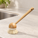 Bamboo-handled kitchen brush with pale bristles beside a sink on a light countertop.