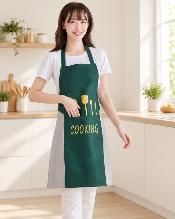 Woman wearing a green apron with grey side panels and yellow COOKING print in a bright ivory kitchen.