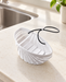 White shell-shaped sink basket with black lanyard beside a kitchen sink.