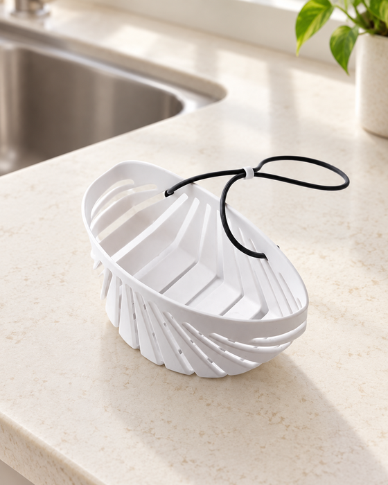 White shell-shaped sink basket with black lanyard beside a kitchen sink.