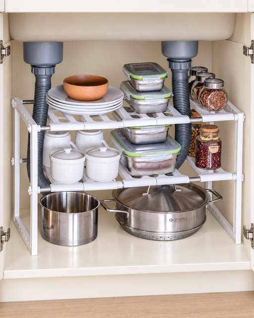 White two-tier kitchen rack arranged around pipes inside a cabinet.