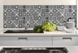 Black and white patterned kitchen backsplash behind a sink, faucet and stacked dishes.