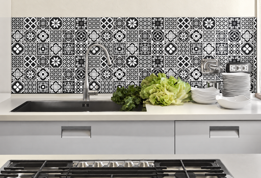 Black and white patterned kitchen backsplash behind a sink, faucet and stacked dishes.