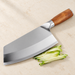 Steel slicing knife with wooden handle and cucumber strips on an ivory surface.