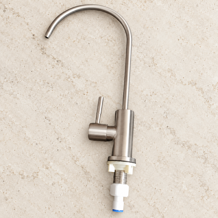 Stainless steel faucet with its mounting connector resting on an ivory worktop.