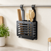 Dark hanging utensil rack holding wooden kitchen utensils against an ivory wall.