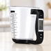 Transparent measuring cup with a black digital scale handle on an ivory counter.
