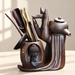 Brown ceramic tea accessory set with sculpted hand, small Buddha and wooden tools.
