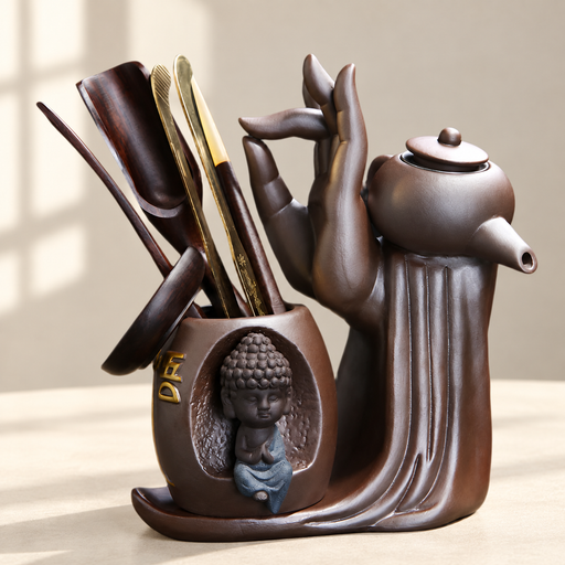 Brown ceramic tea accessory set with sculpted hand, small Buddha and wooden tools.