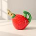 Red strawberry-shaped ceramic oil dispenser with green handle and gold spout.