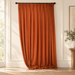 Burnt-orange curtain with pinch pleats and pooled hem in an ivory room.