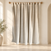 Off-white tab-top curtain hanging from a wooden rod in an ivory room.