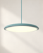 Blue-green disc pendant light with a softly illuminated underside against an ivory wall.