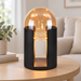 Black table lamp with an amber glass dome on a wooden side table.