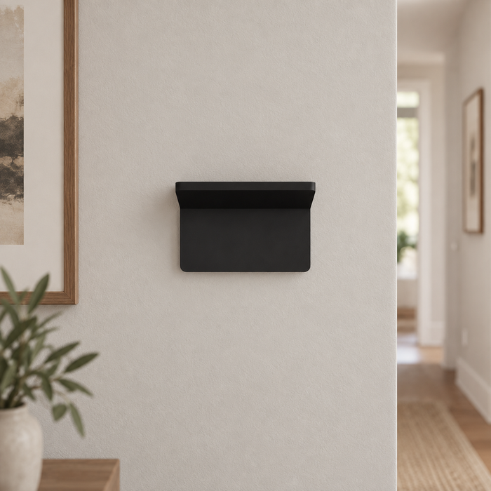 Compact matte black wall light mounted on a pale hallway wall.