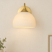 Gold-coloured wall light with a white ribbed glass shade on a neutral wall.