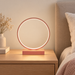 Rose-gold circular LED table lamp on a wooden bedside table.