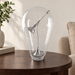 Clear glass art lamp on a dark wood side table.