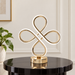 Gold-tone four-loop table lamp on a black side table.