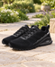 Black running shoes with white side outlines, textured knit uppers and dark sculpted soles on a stone path.