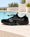 Black mesh water shoe with grey overlays and orange lettering on a pale poolside terrace.