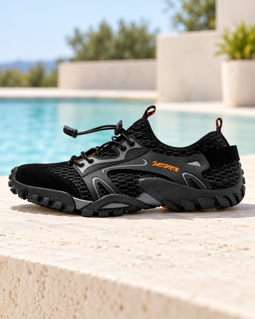Black mesh water shoe with grey overlays and orange lettering on a pale poolside terrace.