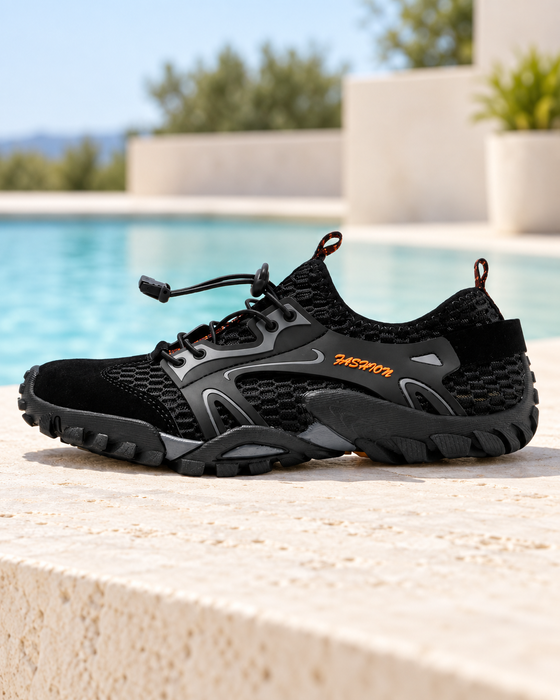 Black mesh water shoe with grey overlays and orange lettering on a pale poolside terrace.