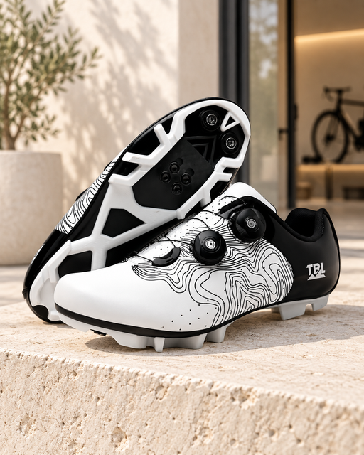 White and black patterned cycling shoes with dial closures, showing the upper and sole on a pale stone ledge.