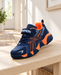 Navy and orange children's sneaker with a fastening strap on a pale wooden bench.