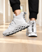 White knit sneakers with open lattice soles worn with black trousers in a bright hallway.